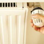 Close-up of hand adjusting radiator thermostat to control home heating temperature.